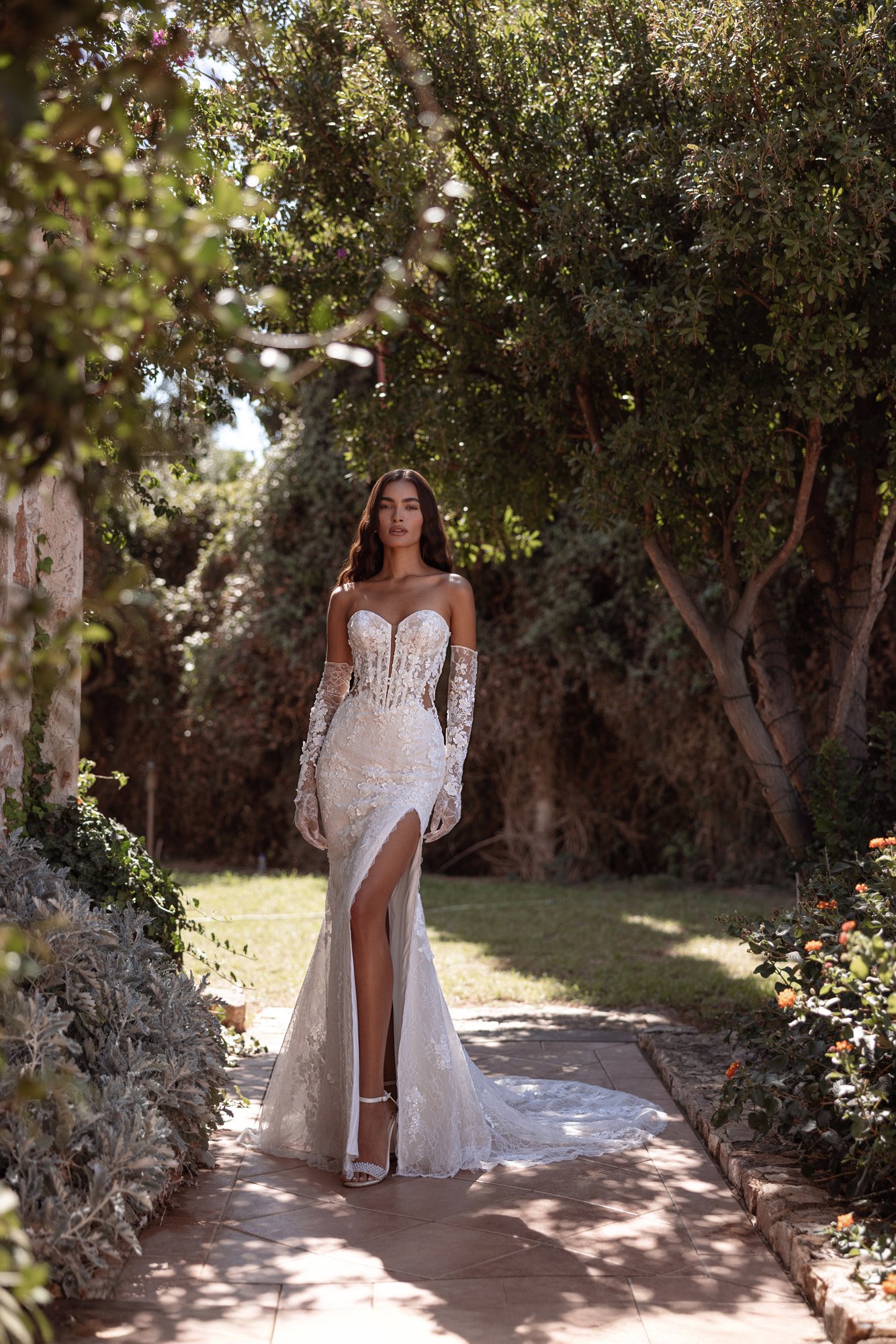 Robe de mariée Cosmobella 8297 à motifs floraux et jupe fendue, présentée avec de longs gants.